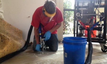 A Ram Jack worker injecting polyurethane foam into cracks or voids in concrete.